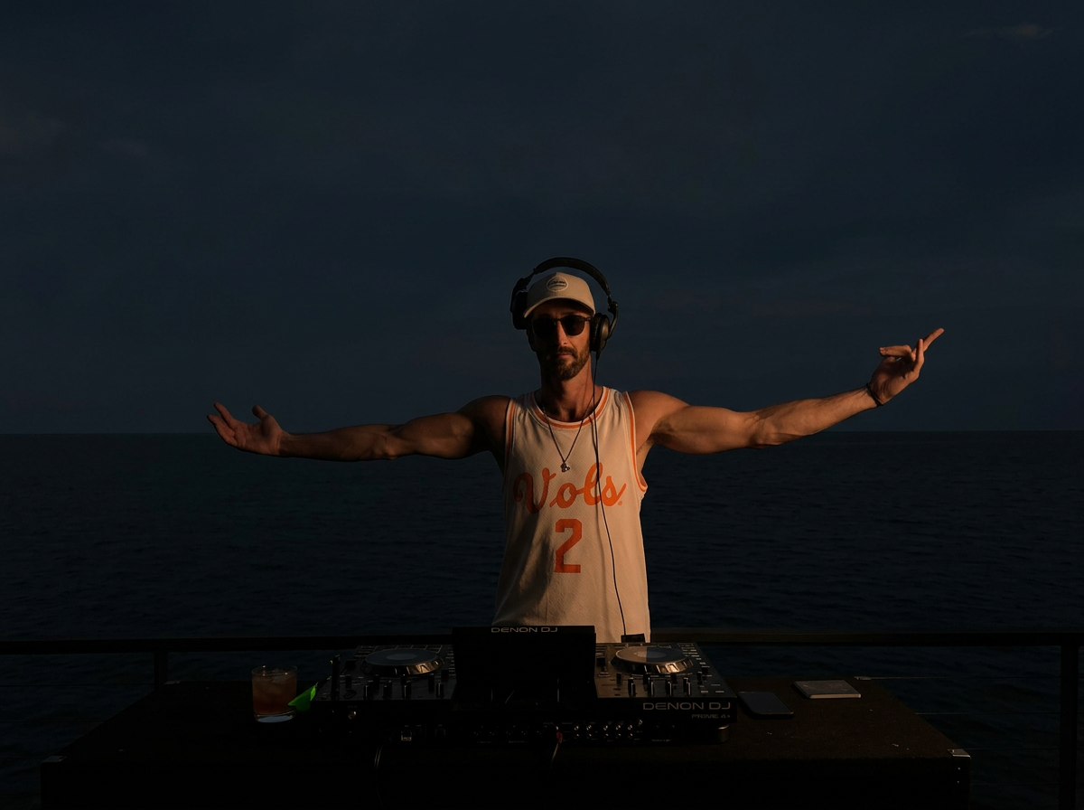 Kylito wearing headphones behind his DJ decks on the water at night